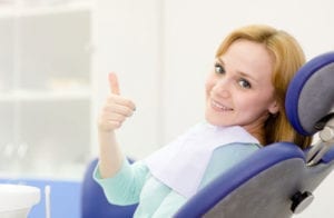 woman in a dental chair giving the thumbs up sign